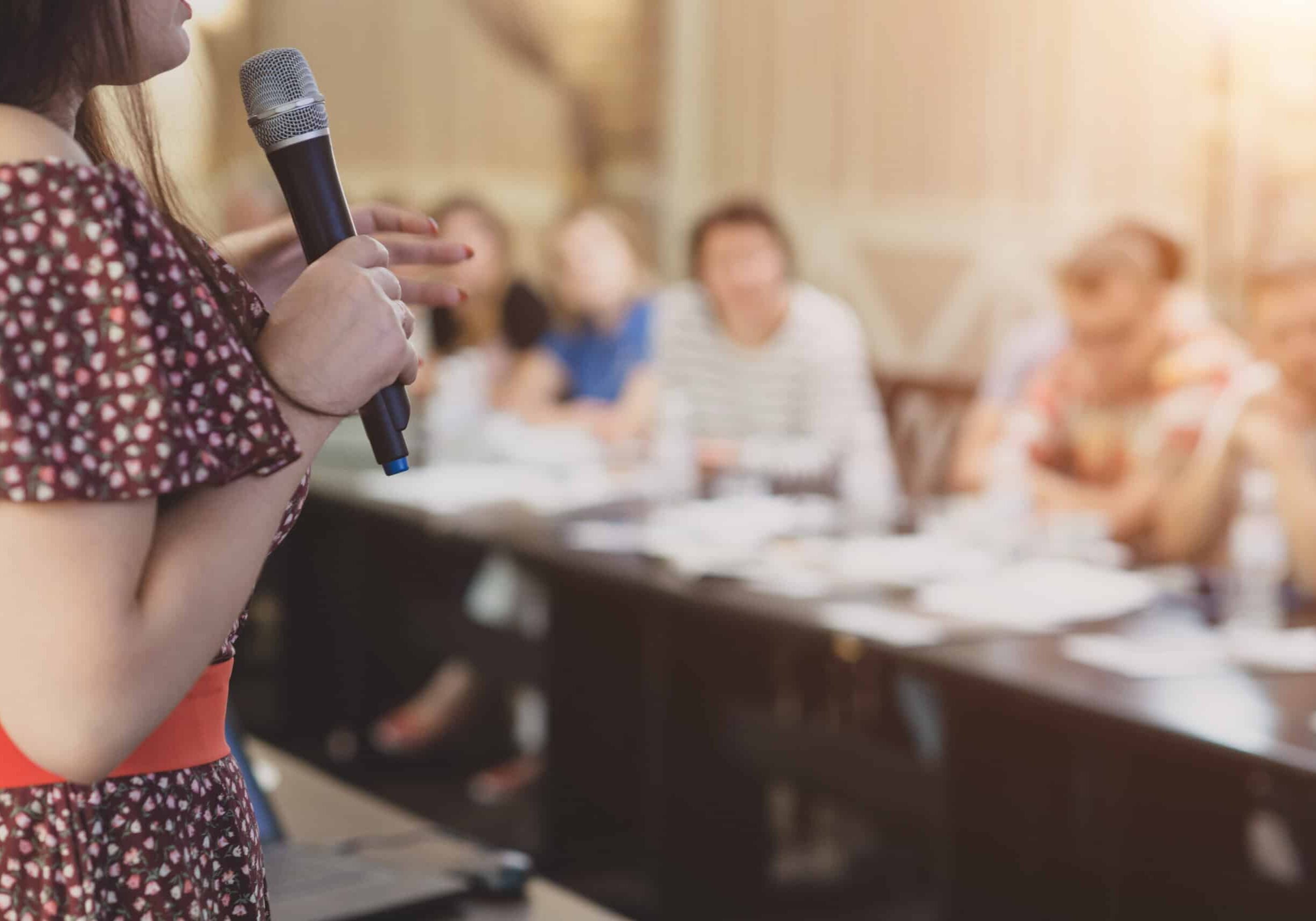 Woman with microphone speaks to the public.